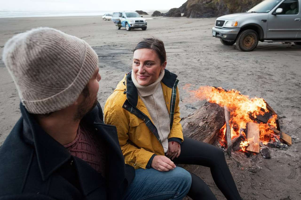 A man and woman enjoy a campfire on the sand in the Washington Beaches Region