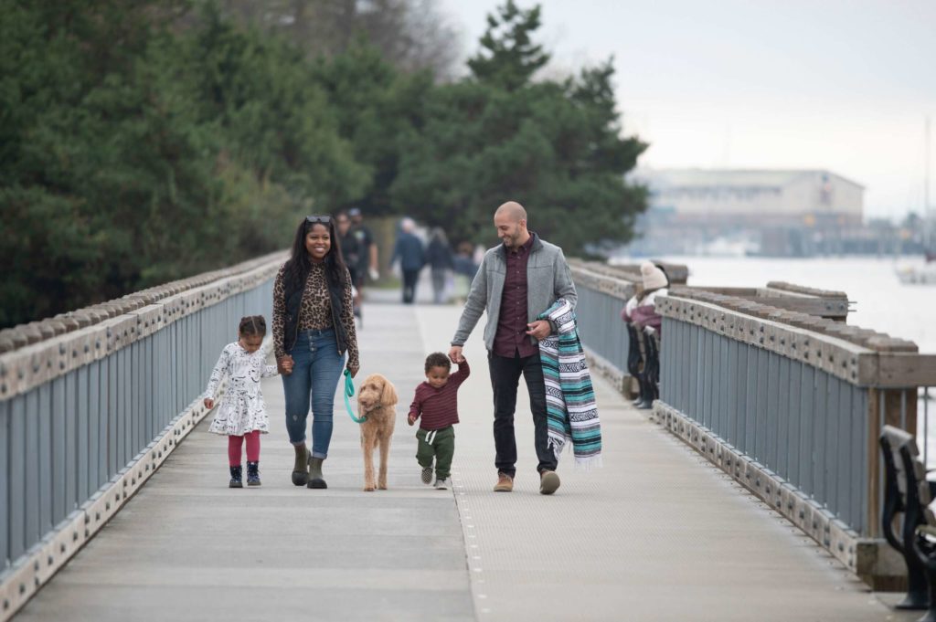 Mom and dad walking along the water with their two kids and a dog