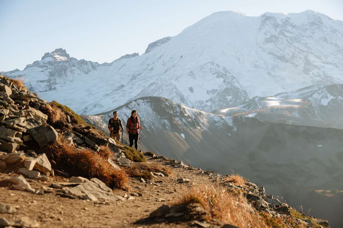 Two people hiking along trail in the Volcanoes Region with Mount Rainier in the background.