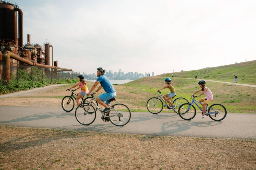 A mother, father, and two children ride bikes past Gas Works Park in Seattle.