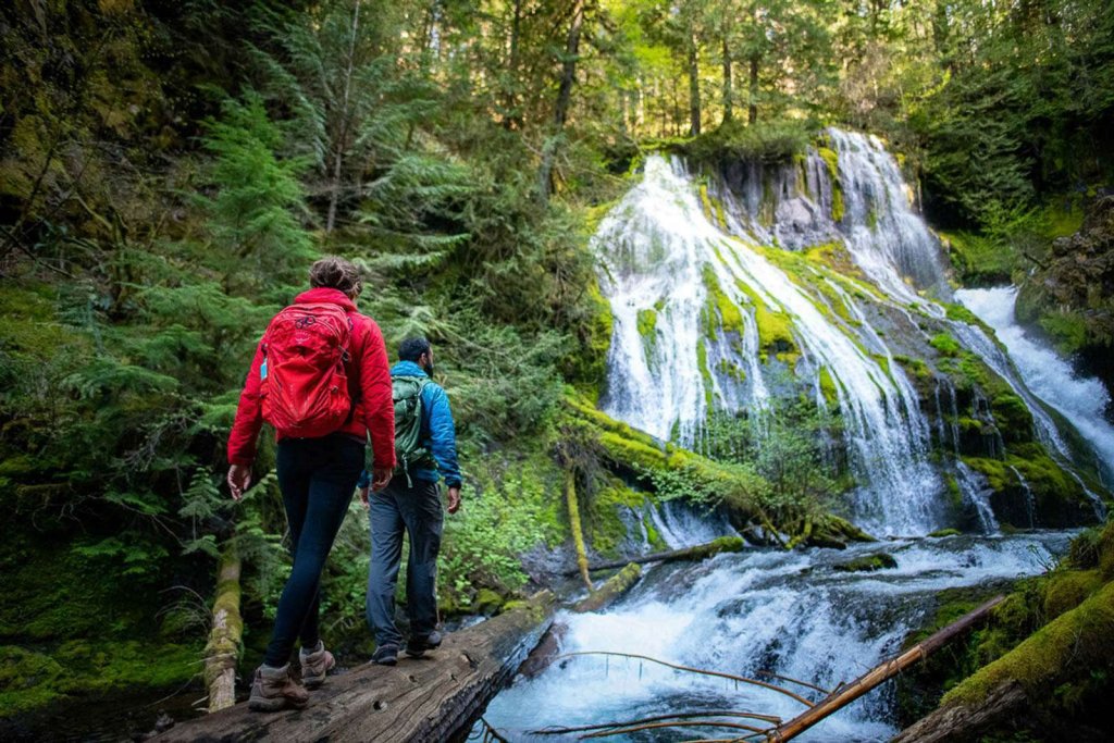 Two people stand at the base of Panther Creek Falls in Washington