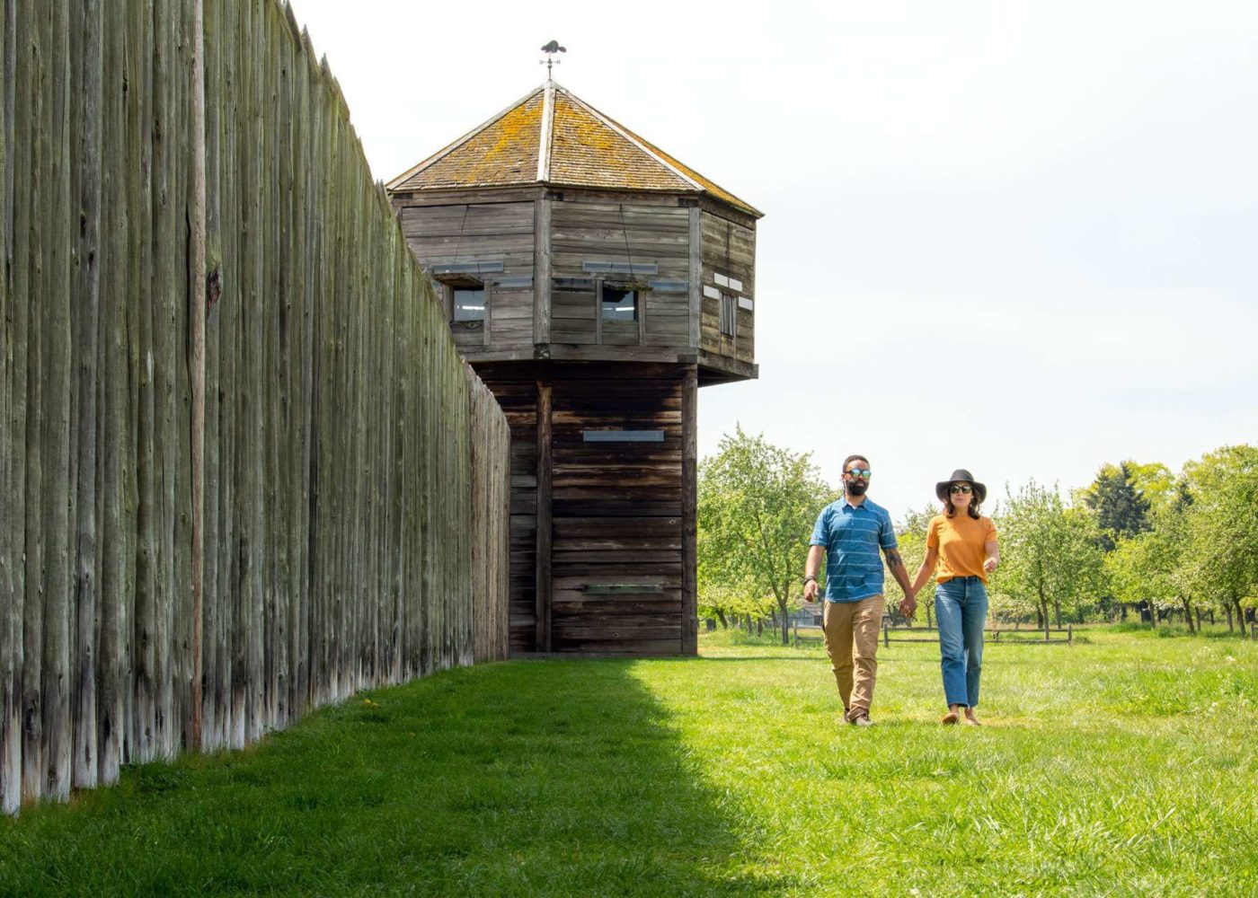 Couple holding hands walking along a wooden wall at Fort Vancouver
