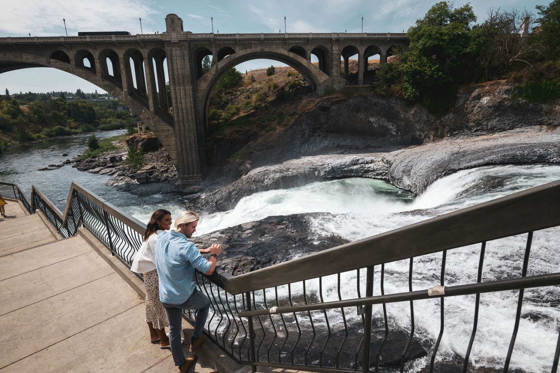 Man and woman leaning against railing looking out over Spokane Falls-Take a Ponderosa Washington Vacation