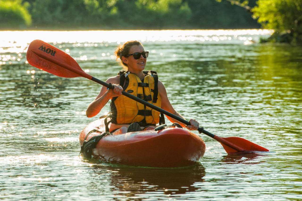 A woman wearing sunglasses and a yellow lifejacket enjoys kayaking in Washington on the Spokane River.