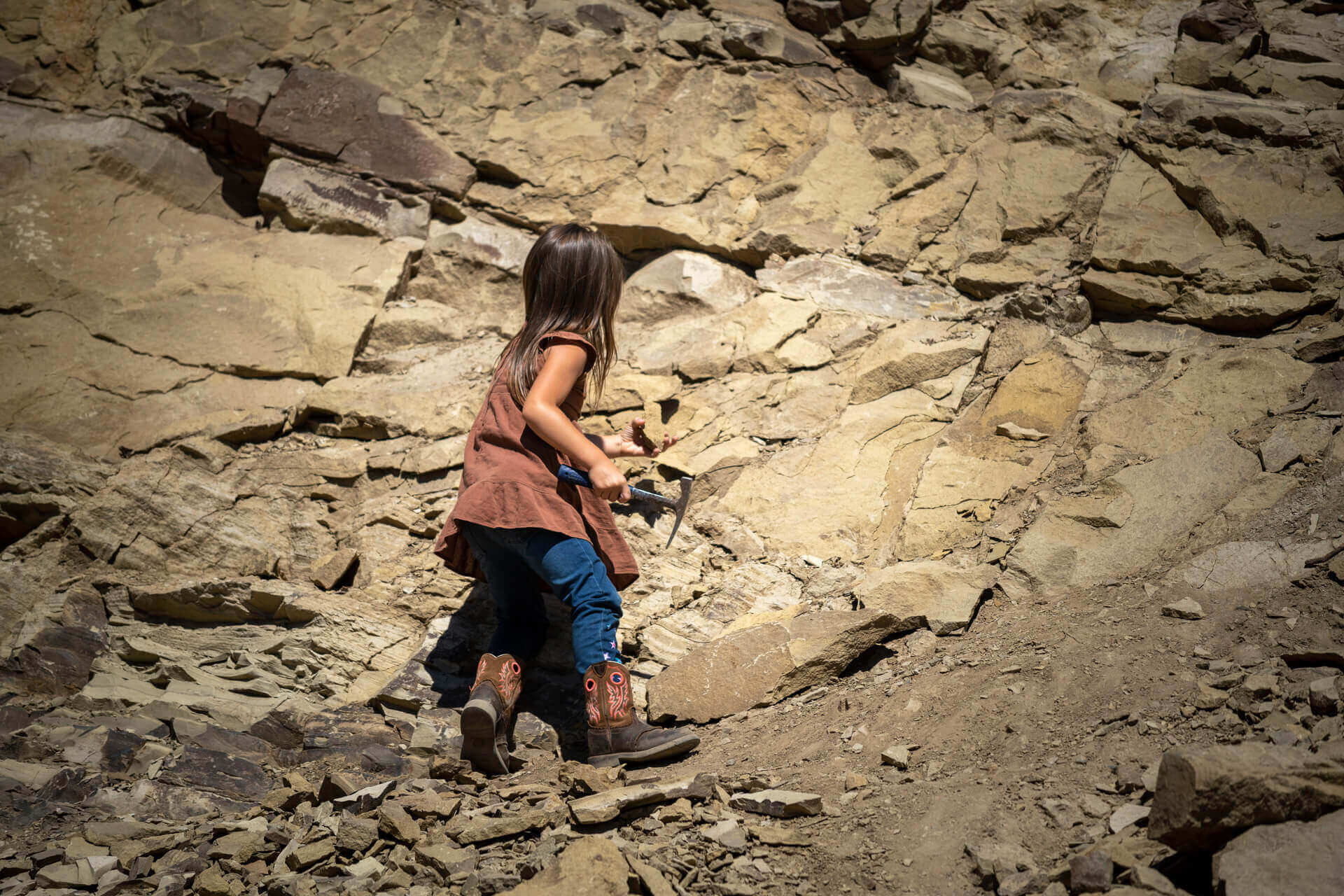 A young girl chips away at a rock face while digging for fossils in Washington, one of many things to do with kids.