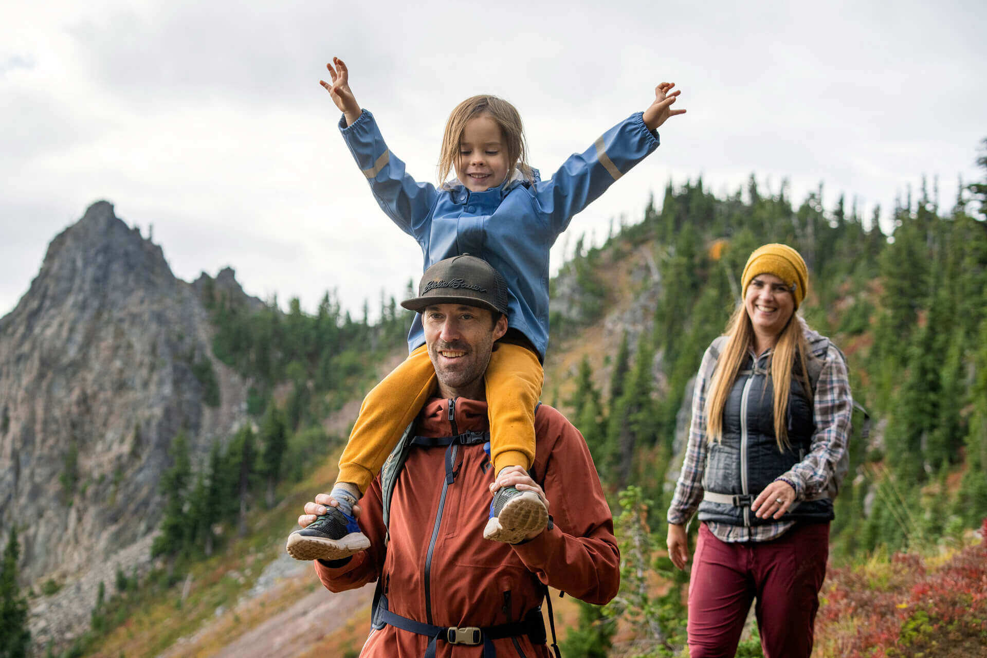 A man carries a girl on his shoulders during a hike. 