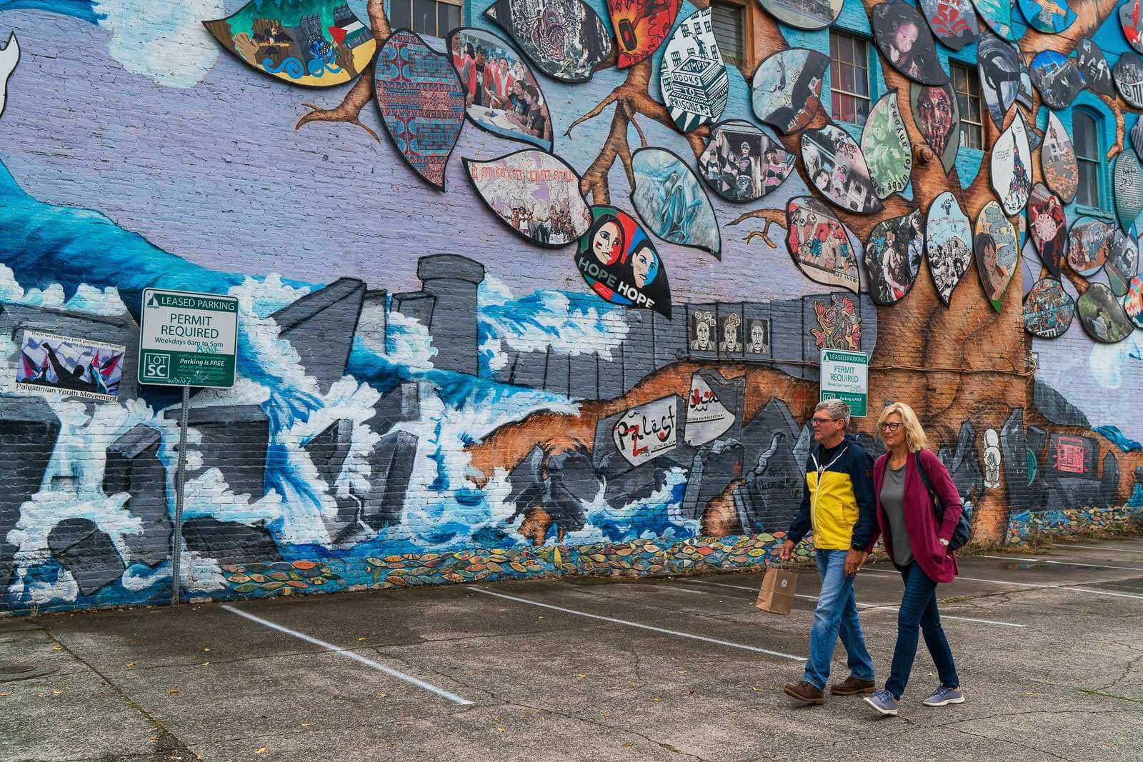 Man and woman hold hands as they walk past a mural in Olympia