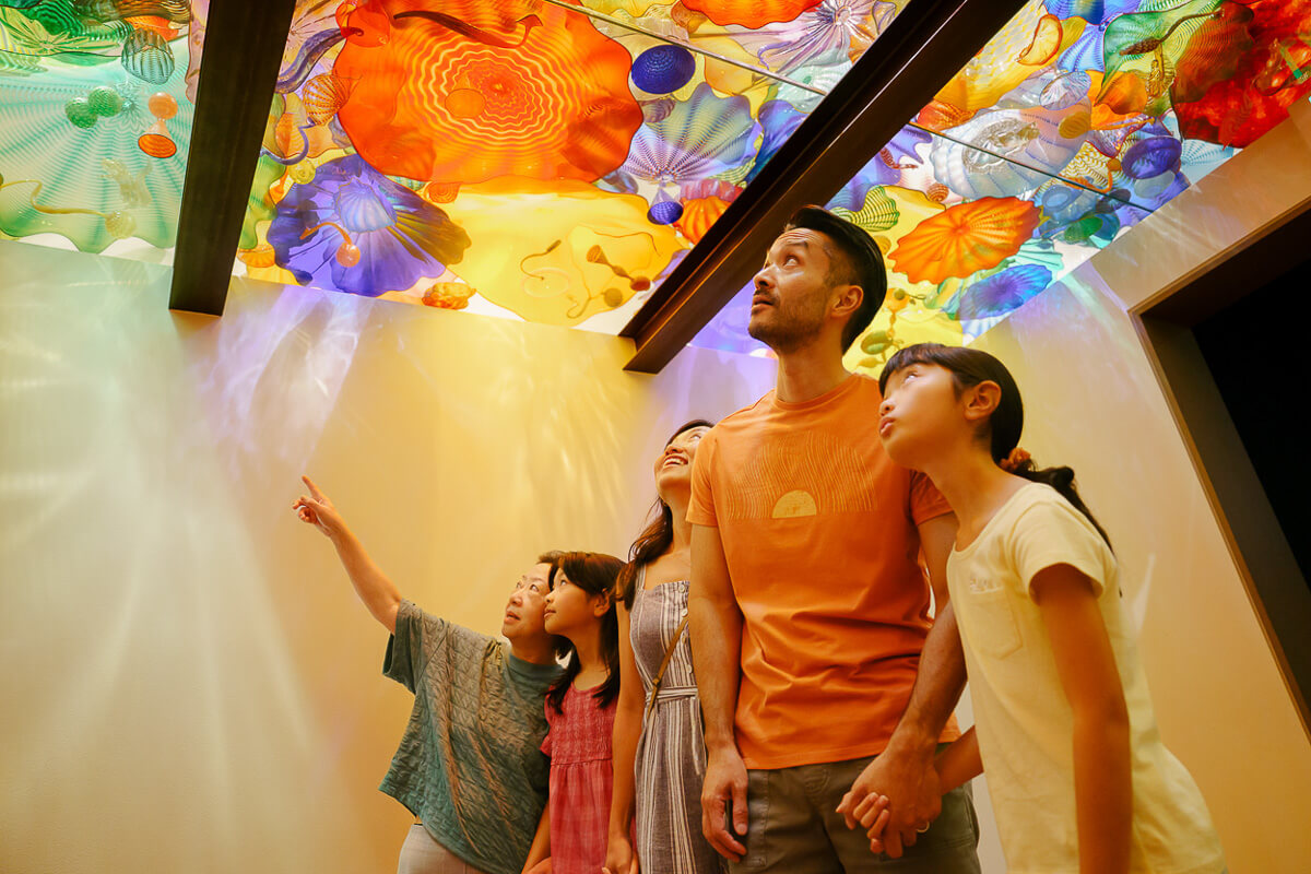 A mother, father, grandmother and two children look up at colorful glass works at Chihuly Garden and Glass in Seattle.