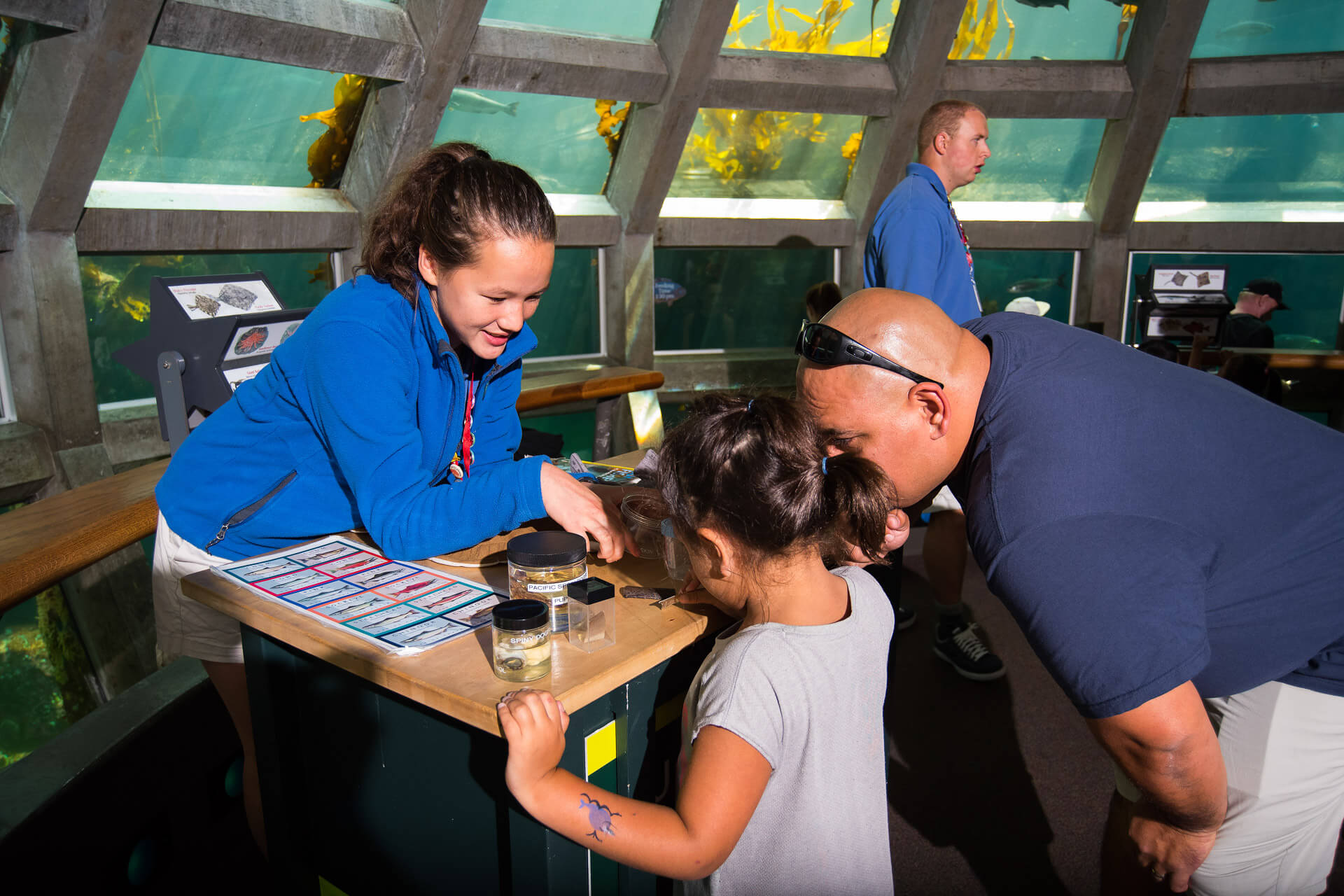 A father and daughter look at fish with the help of a Seattle Aquarium staff member 
