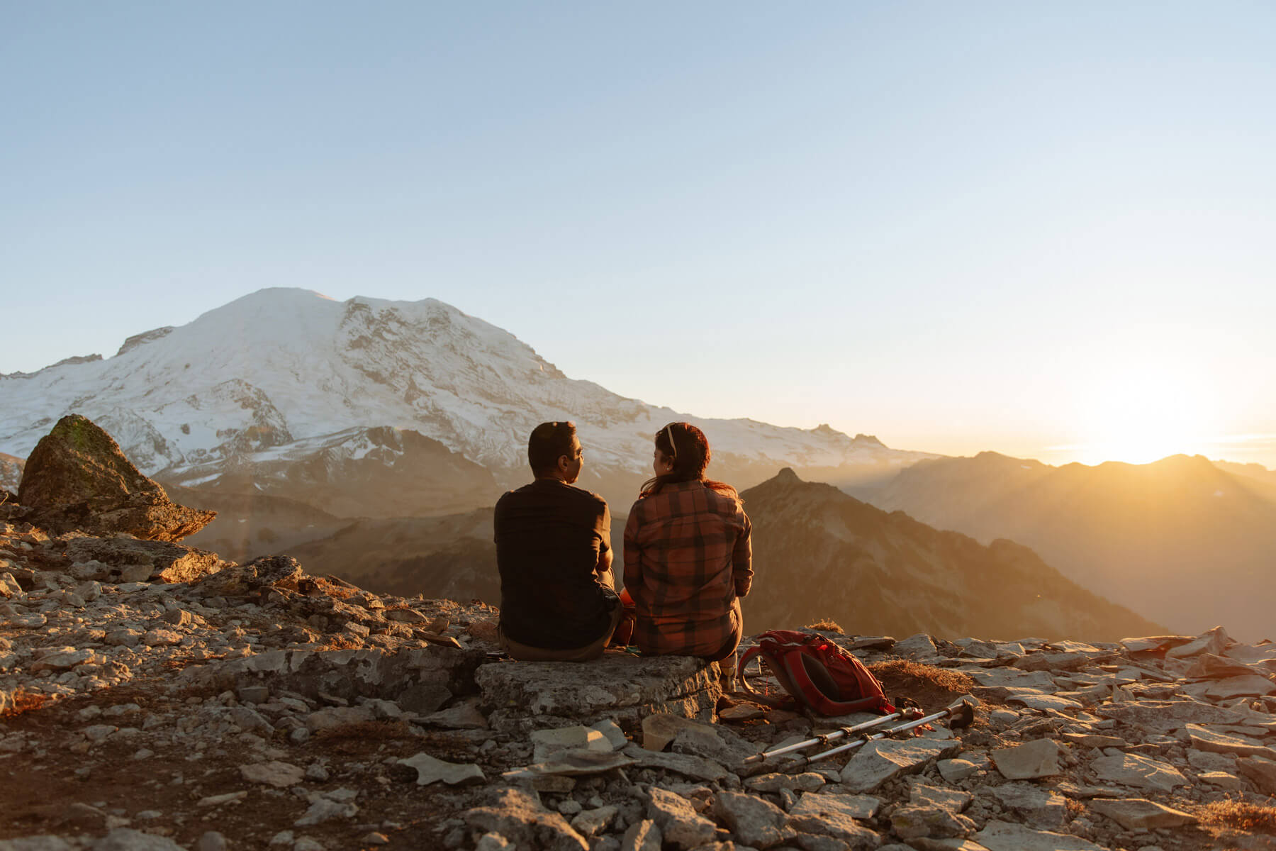 Two people sit on the ground with Mount Rainier in the background