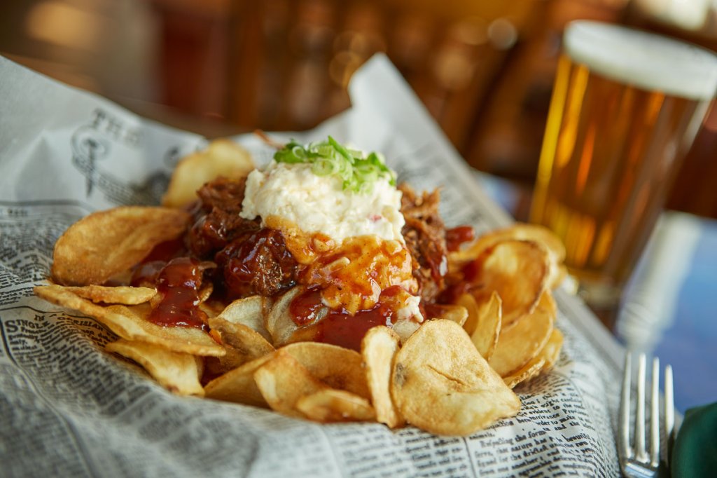 Potato chips are loaded with chili and sour cream in a basket lined with newspaper.
