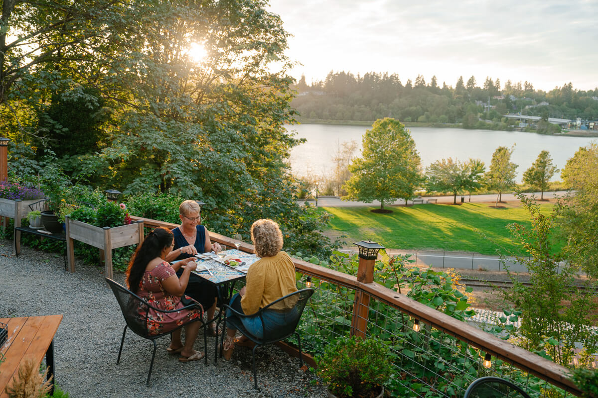 Three women dine outside at a restaurant overlooking a lake. 