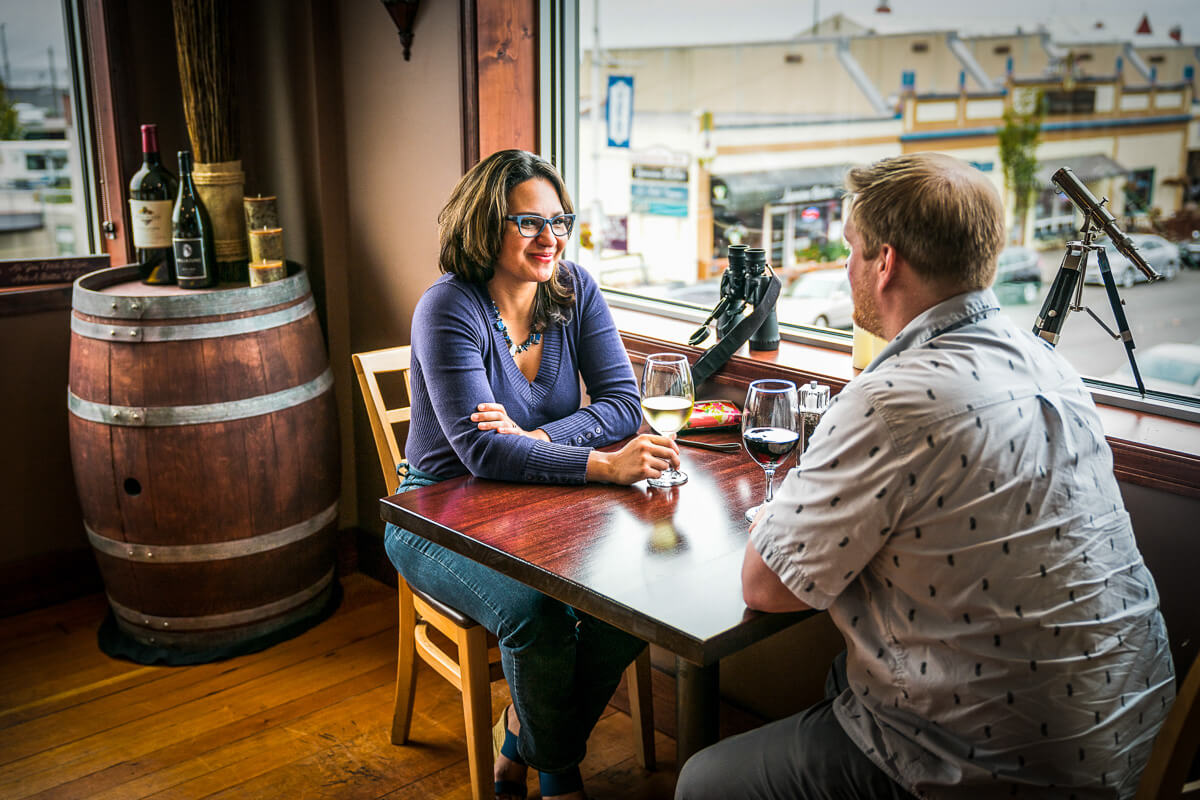 A man and woman sit at a table with glasses of wine