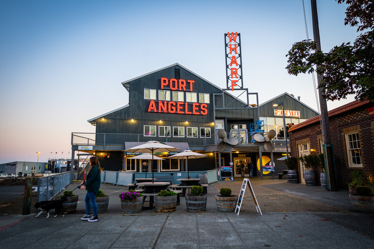 A woman walks her dog in front of the Port Angeles Warf building