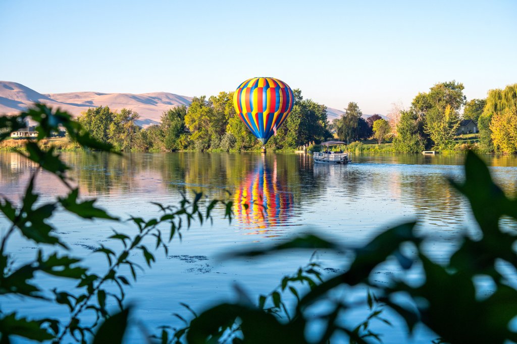 A yellow, blue, and red striped hot air balloon glides over a river in Eastern Washington. 