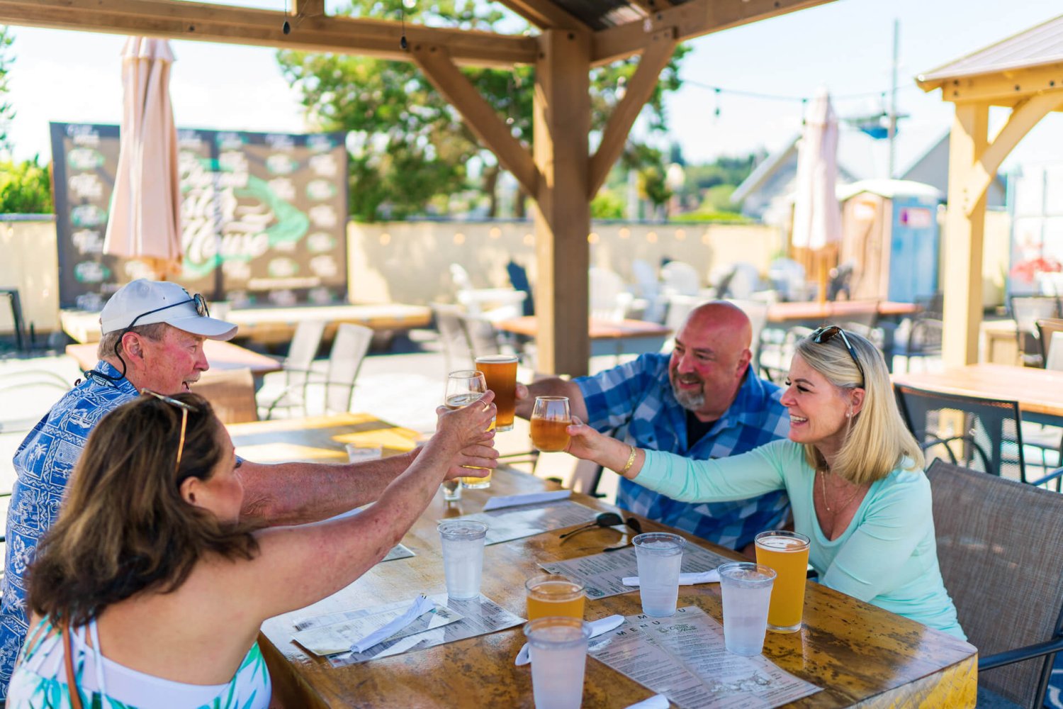 Two couples raise glasses of beer while sitting at an outside picnic table in Olympia.