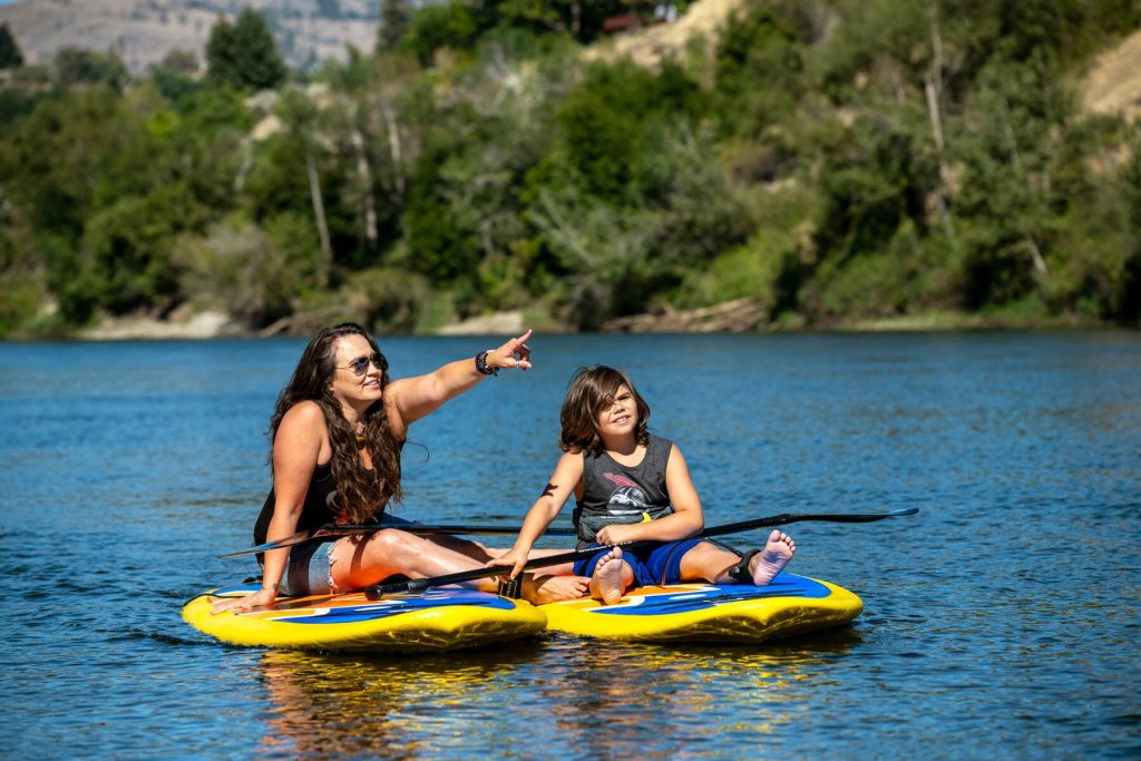 A mother and her son sit on paddle boards.