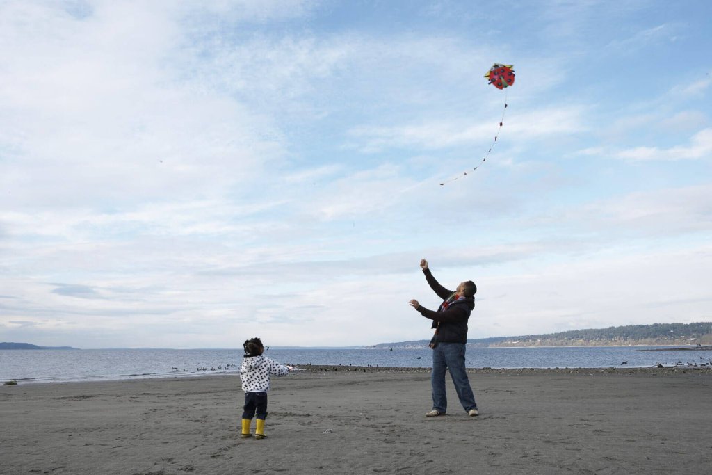 A man shows a small child how to fly a kit on the beach.
