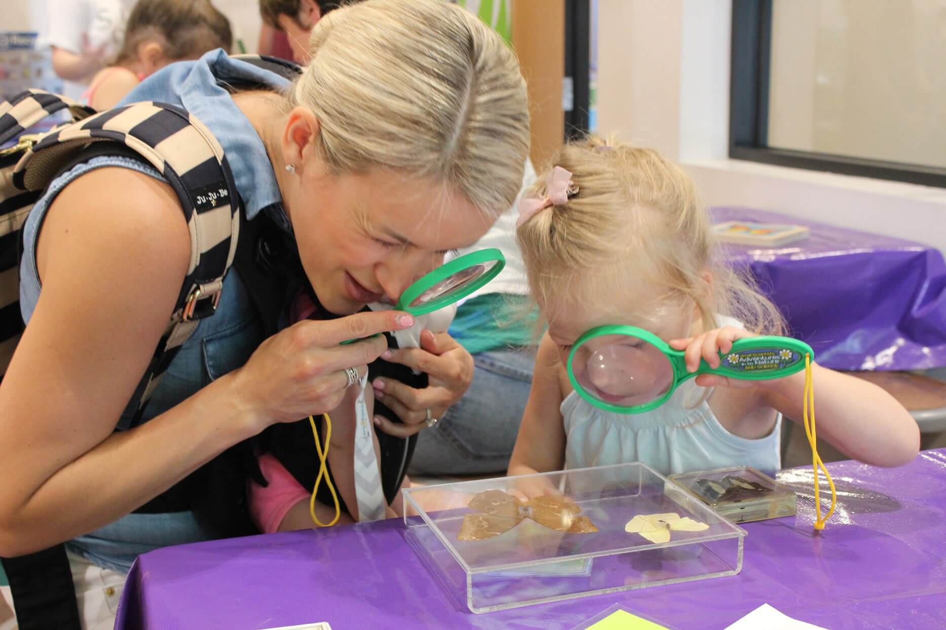 A mother and daughter peer use magnifying glasses to look at rocks