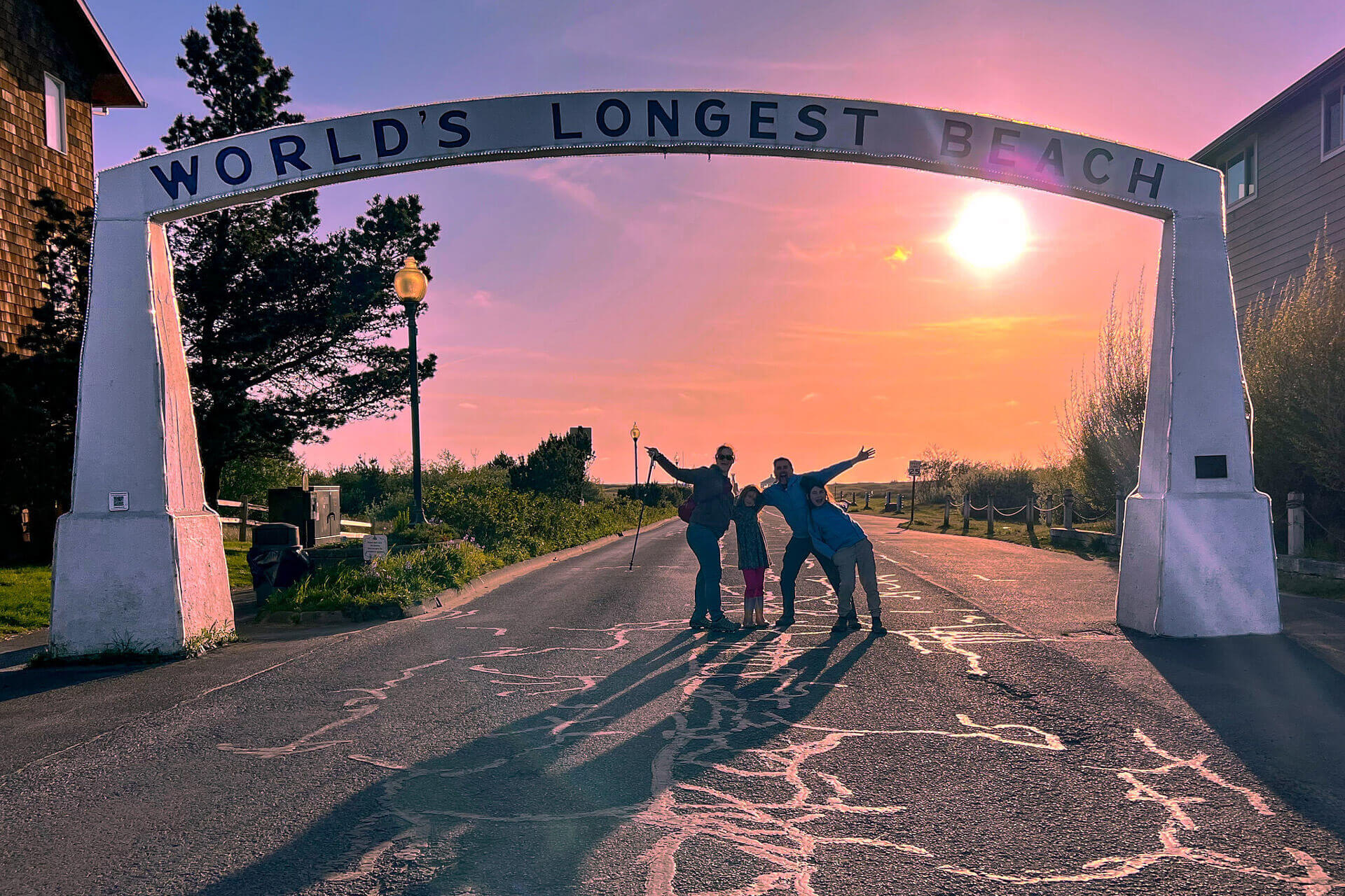 A husband and wife pose with their two children under an arch that reads "World's Longest Beach" during a family trip to Long Beach Washington