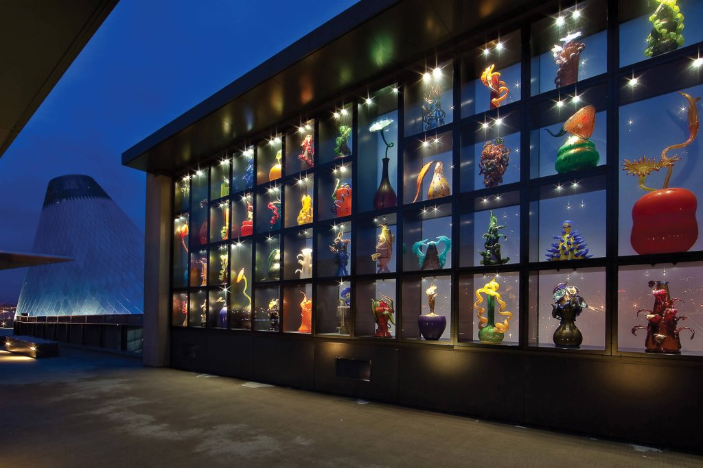 A wall of squares holding colorful glass artworks is seen at night at the Museum of Glass bridge in Tacoma