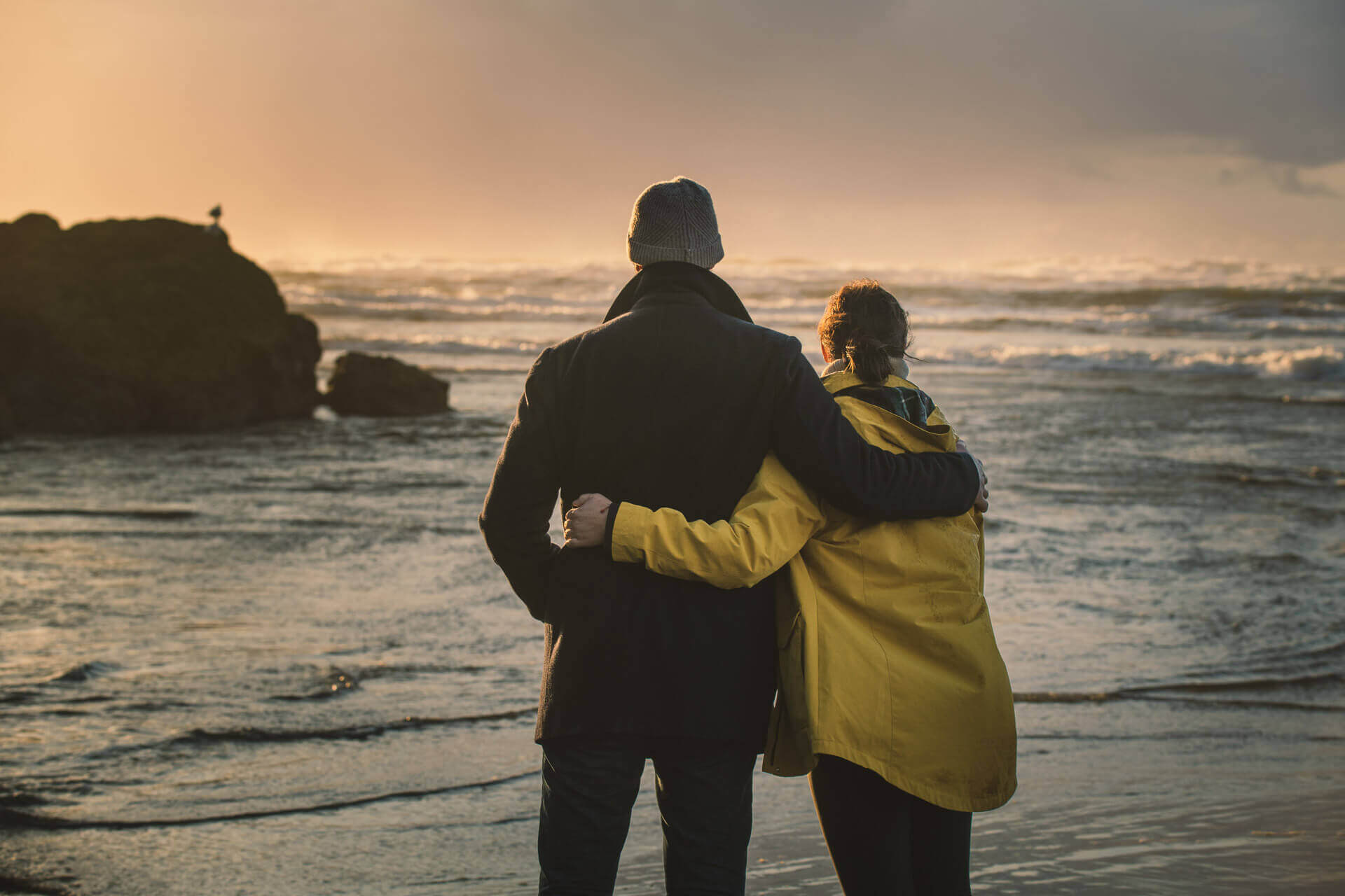 A man and woman stand arm in arm overlooking the waves while storm watching during winter in Washington