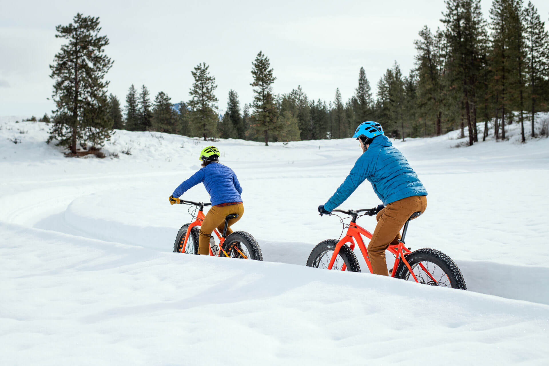 Two people ride along a snow-covered trail on fat-tire bikes