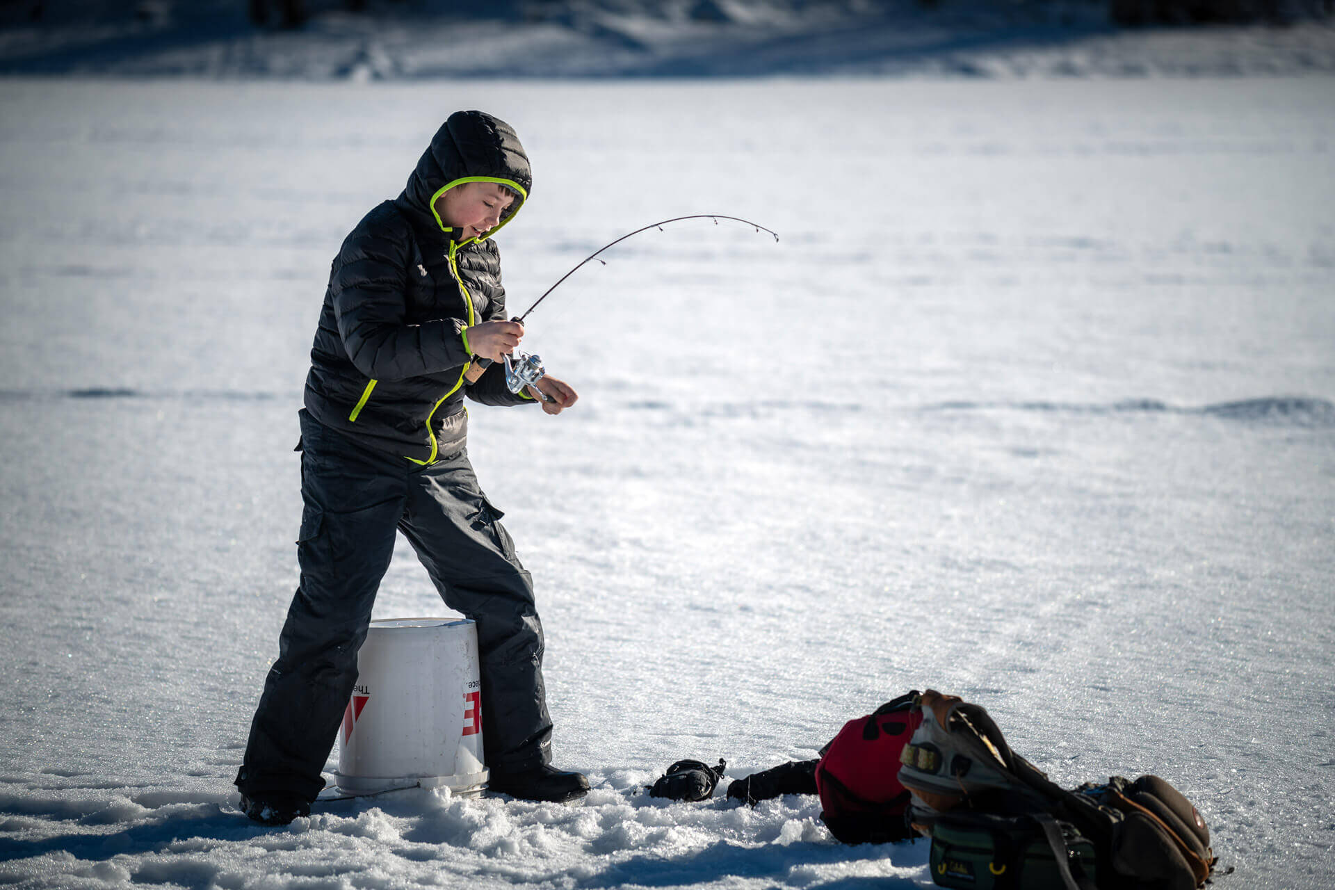 A boy reels in a fish through a whole in a frozen lake during winter in Washington