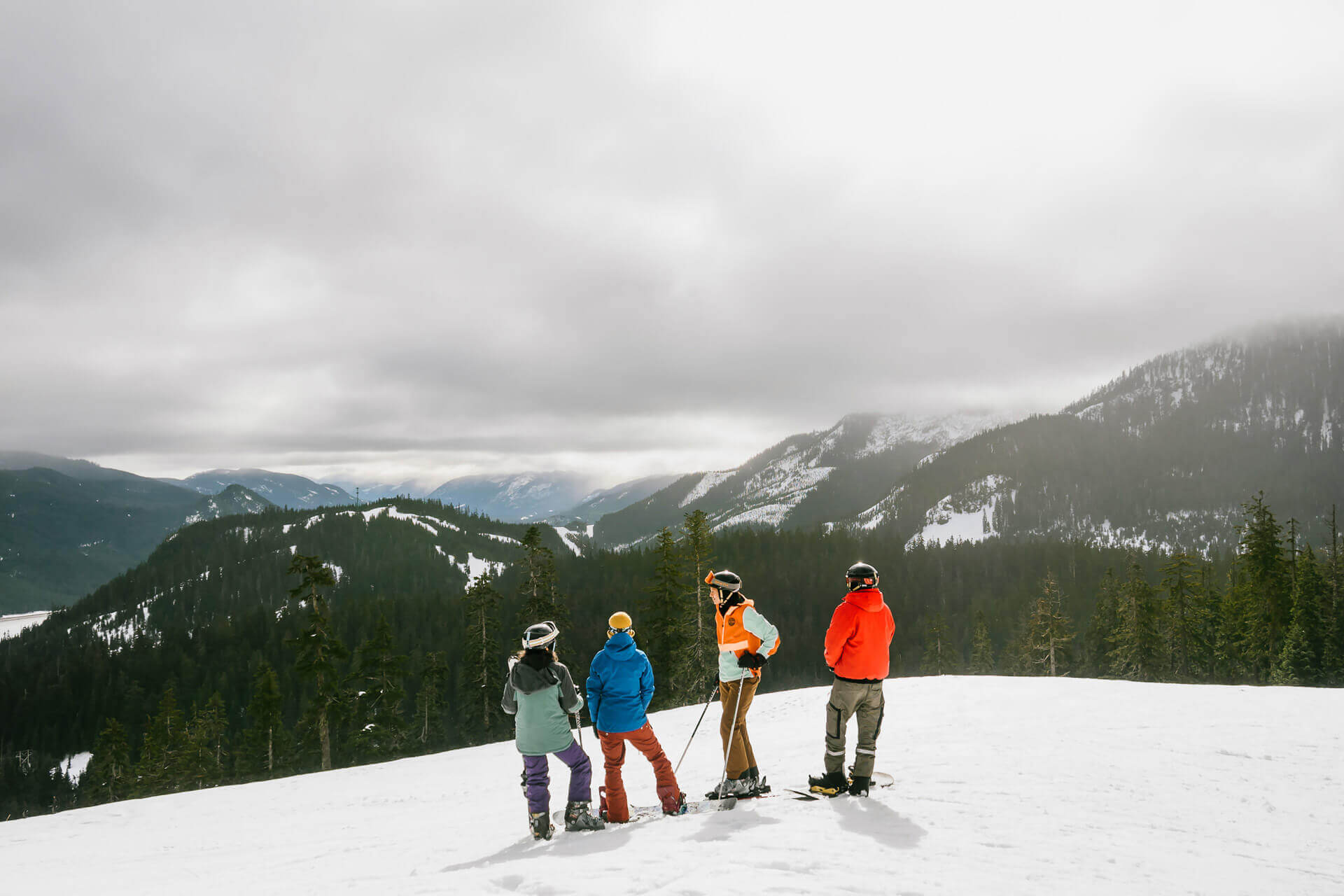 Two couples pause from snowboarding to look over the snowy landscape