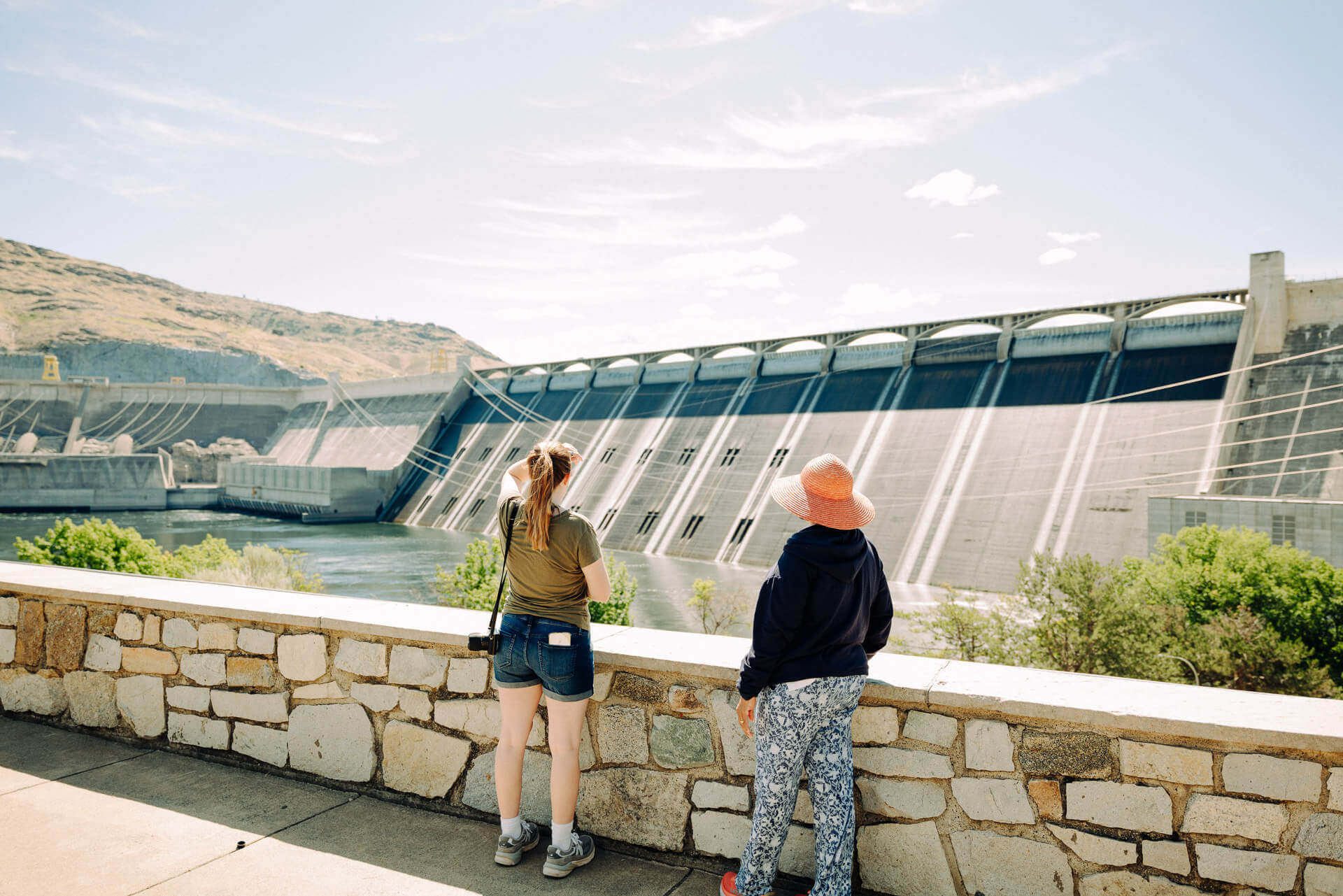 Two women stand along a walkway and look out at the Grand Coulee Dam during an Eastern Washington road trip.