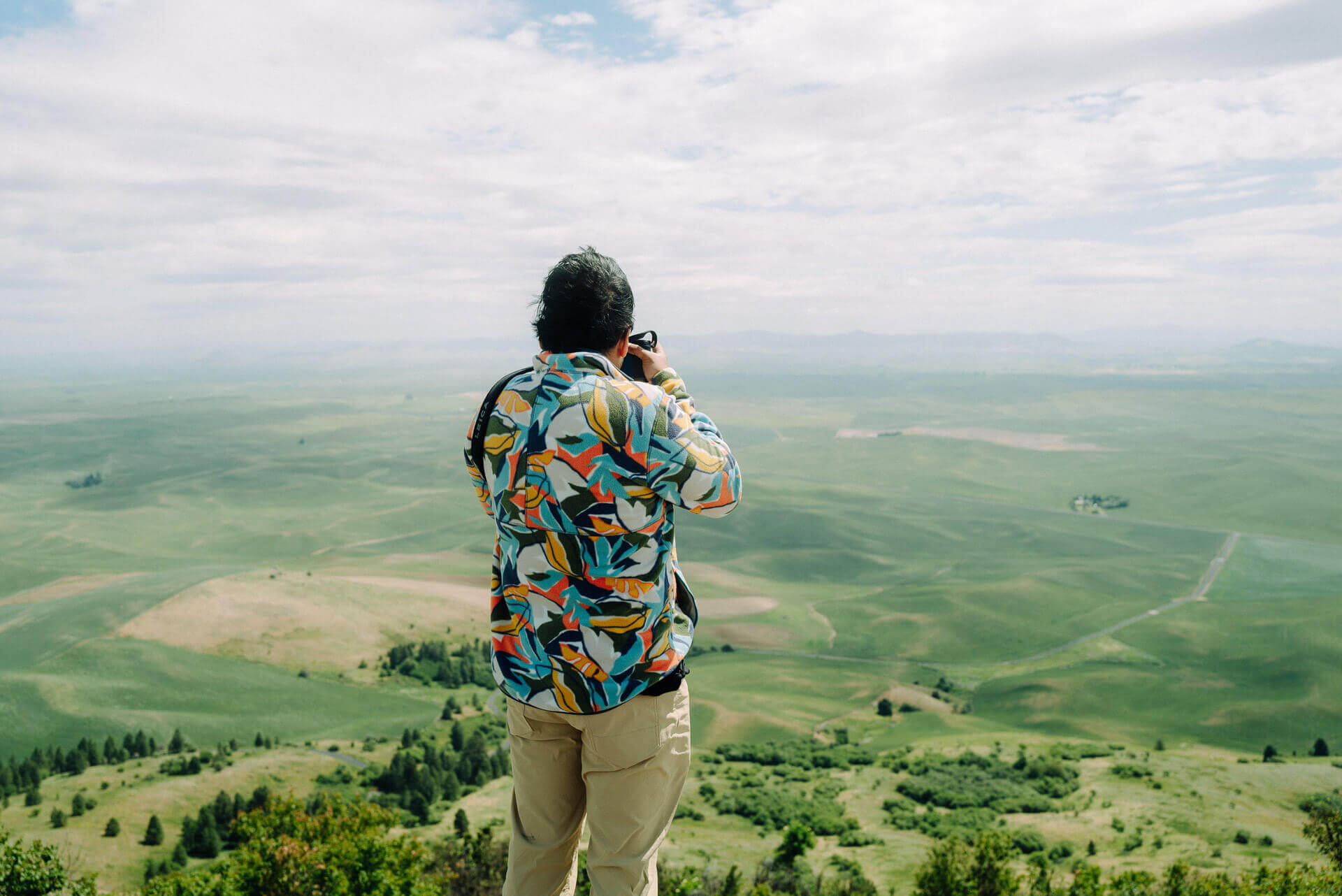 A man takes a photo overlooking rolling green farmland during an Eastern Washington road trip.