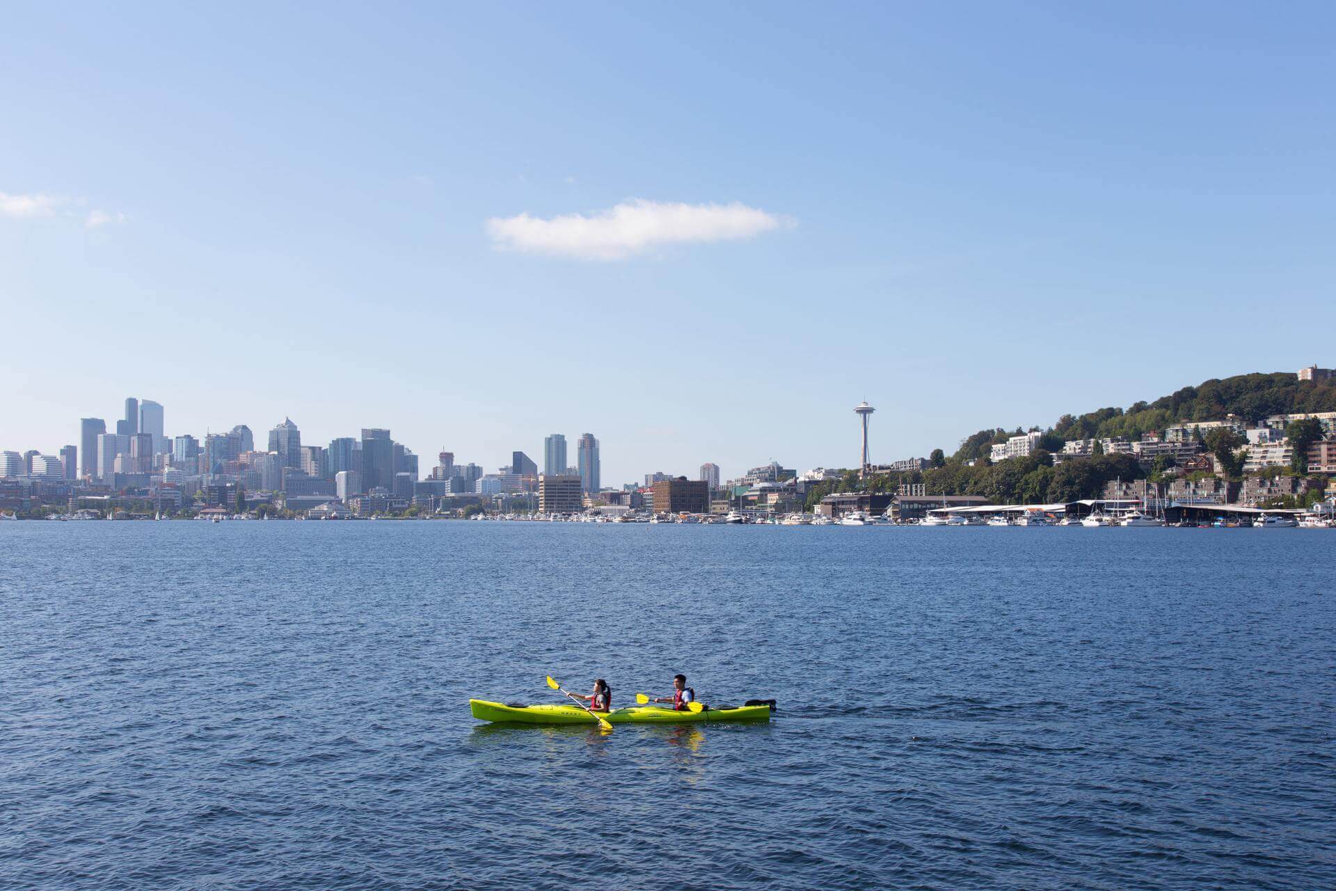 Two people kayak on Lake Washington with the Seattle skyline in the distance.