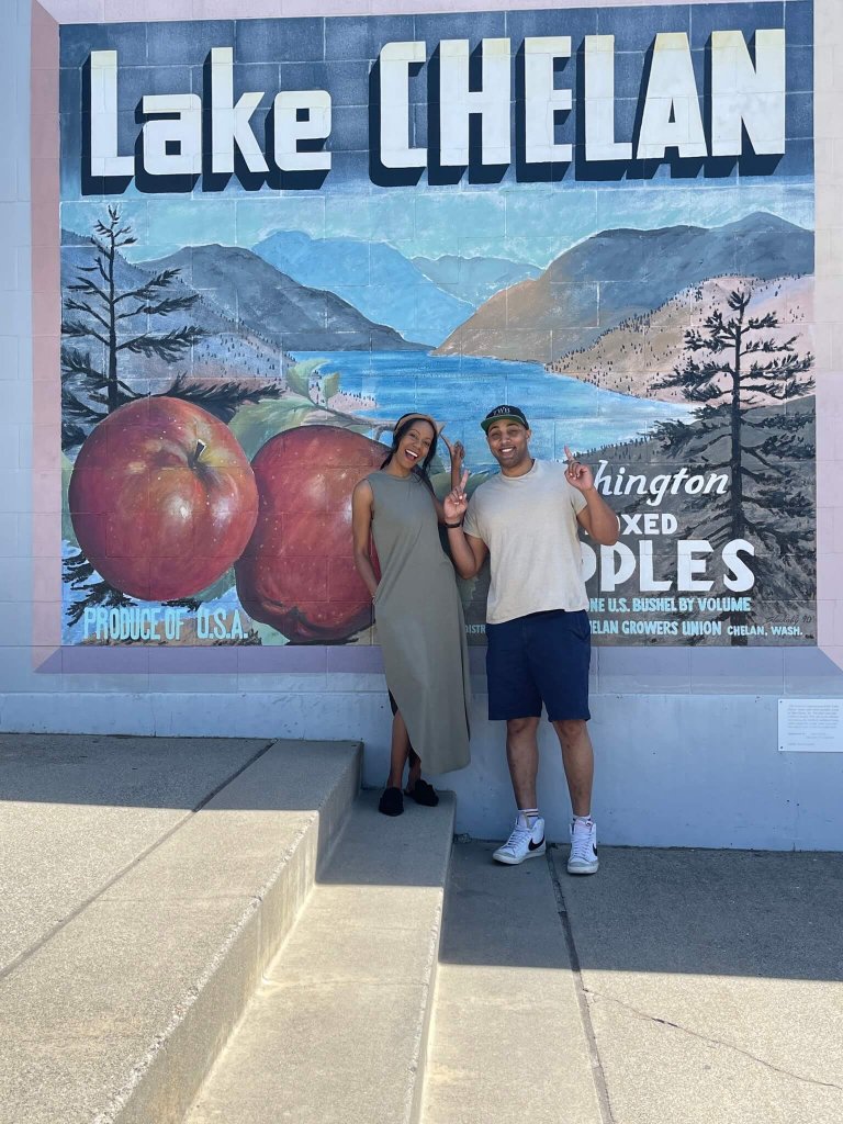 Anthony & Marlie Love pose in front of a mural that reads "Lake Chelan"