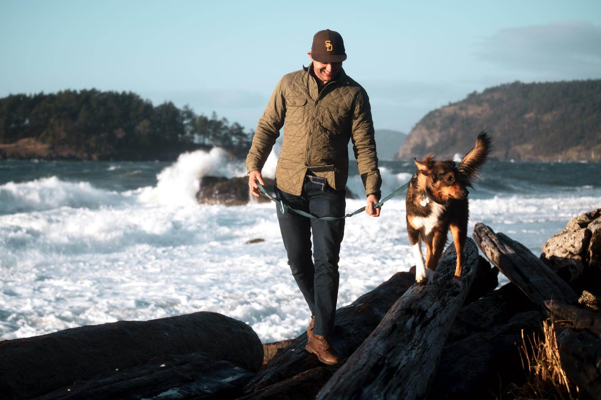 A man walks a dog along driftwood at Deception Pass State Park