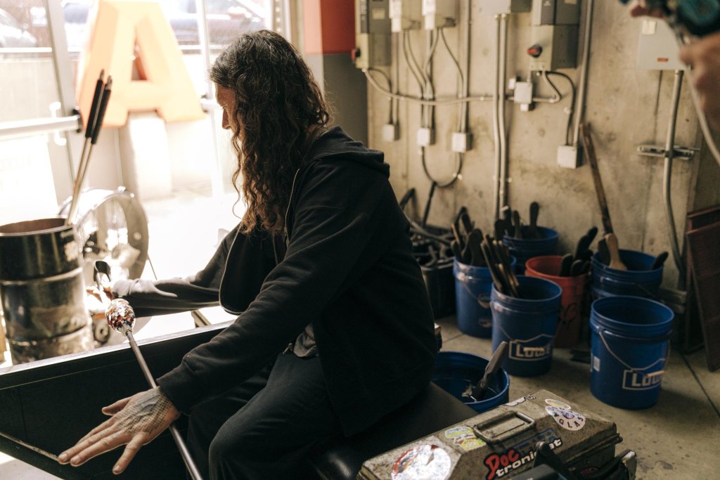 A glass artists uses tongs to shape molten glass into art