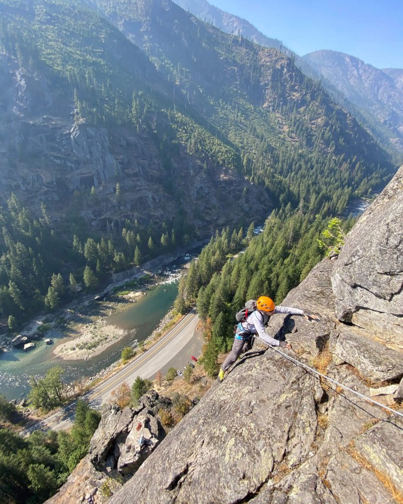 A woman in a helmet and harness climbs a rock face.