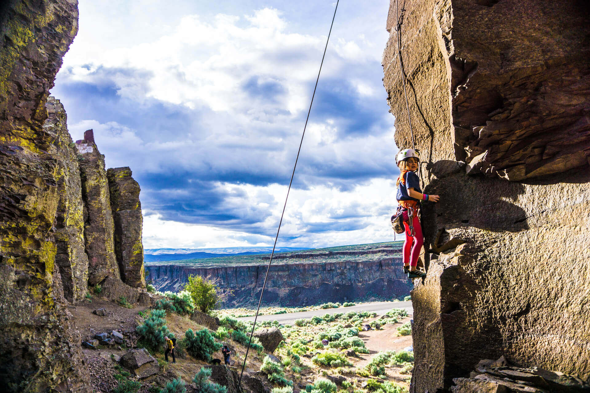 A young girl wearing a helmet and gear perches on a ledge while rock climbing in Washington.