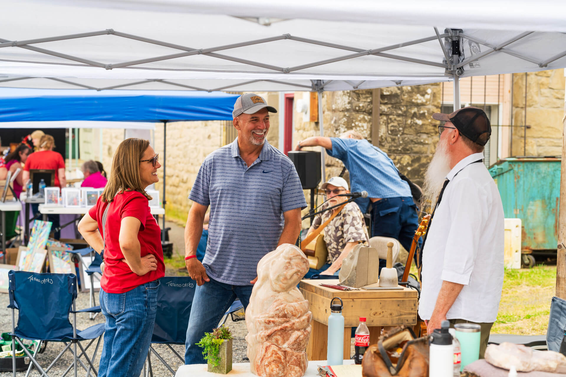 A man and woman speak to a woodcarver at a market