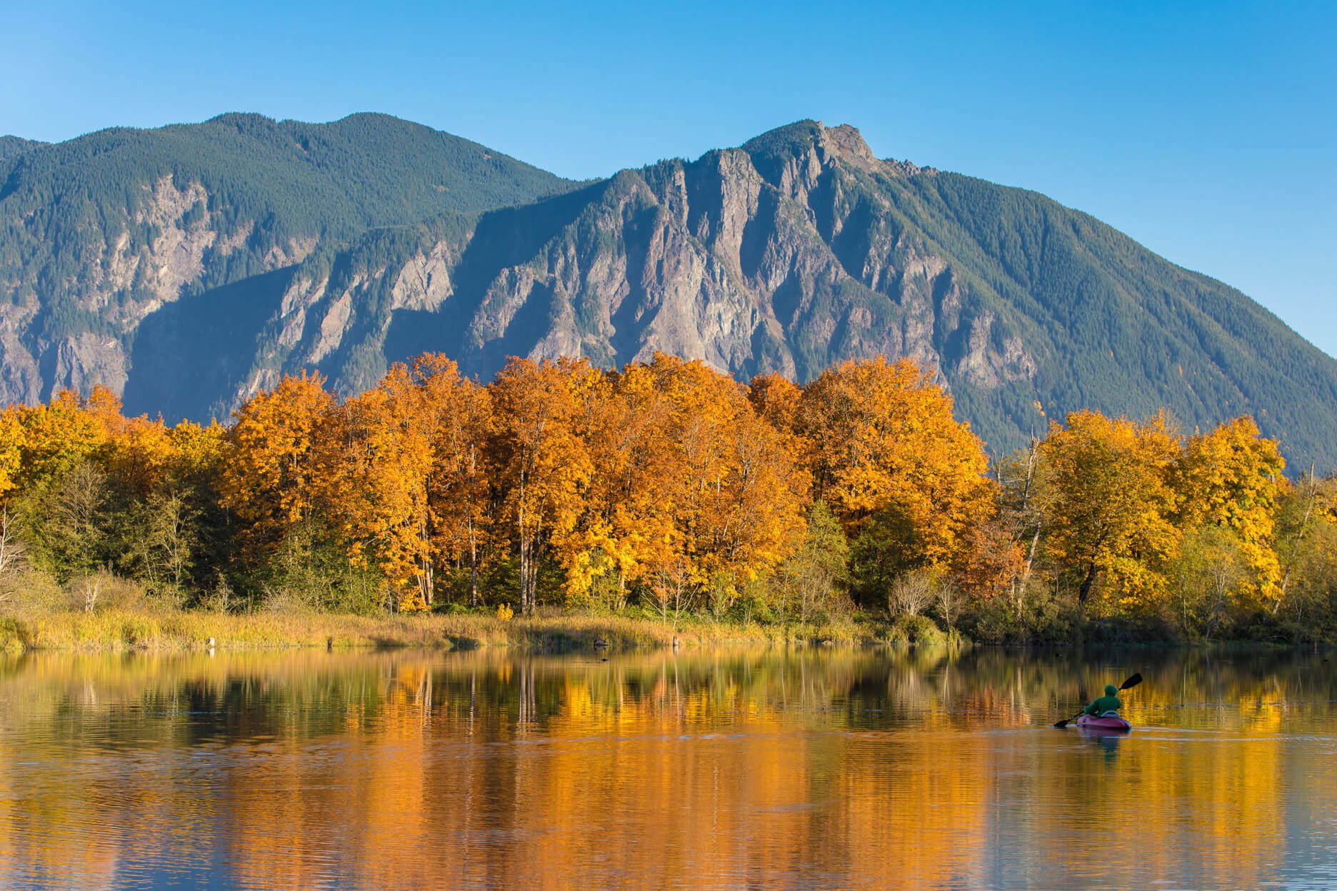 Photo of orange trees along a river with a mountain in the background. Scenic Washington Fall Drives.