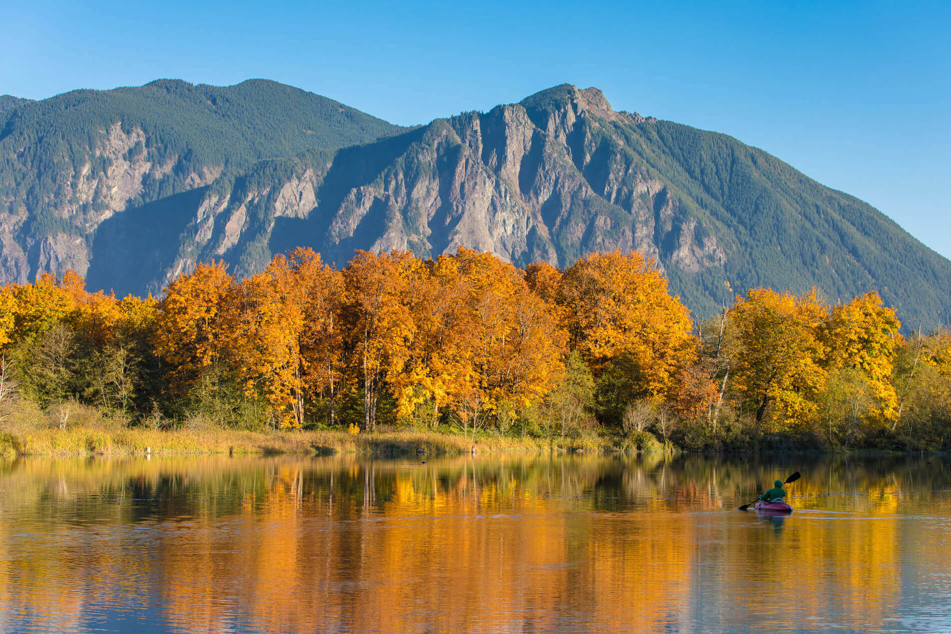 Photo of orange trees along a river with a mountain in the background. Scenic Washington Fall Drives.