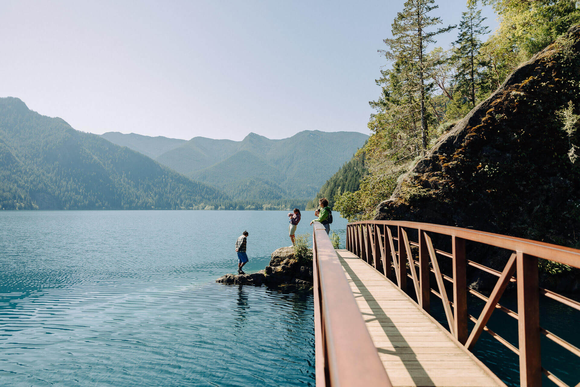 A group of people stand next to a bridge over blue water