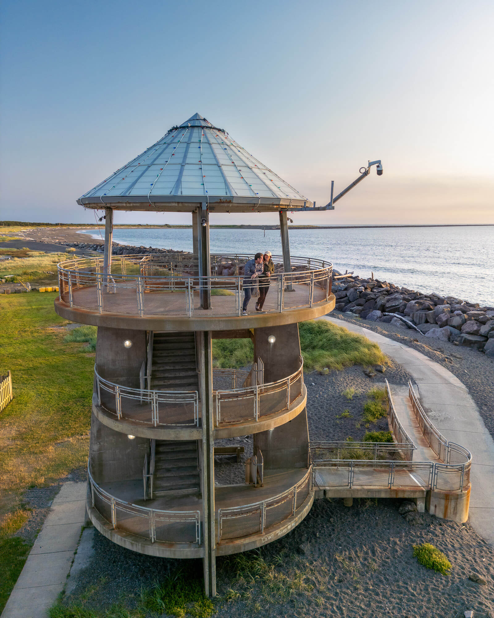 Two people stand at the top level of on observation deck overlooking the ocean in Westport