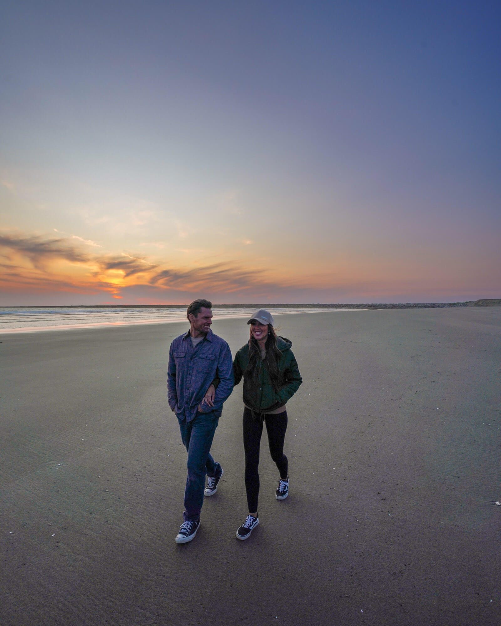 A couple walks along the beach at sunset in Westport