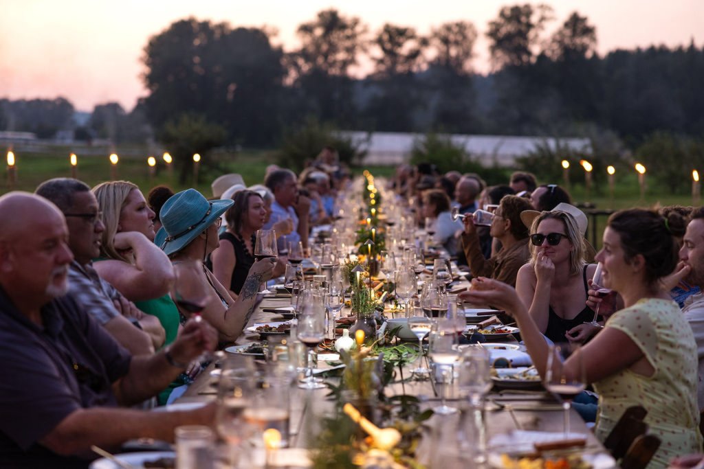 Diners enjoy a meal at a long table in a field at Carnation Farms