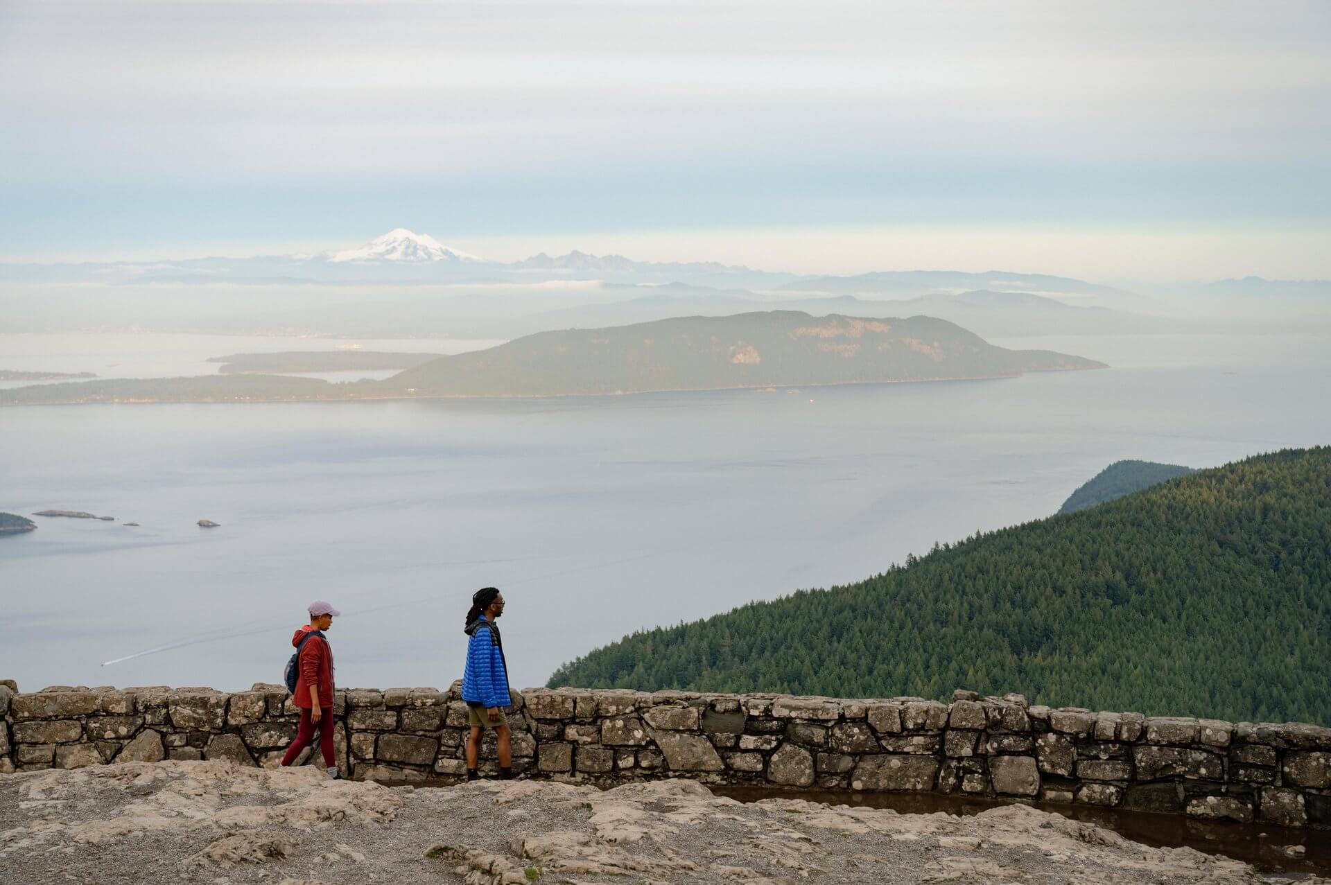 A man and woman walk along a rock wall overlooking the San Juan Islands