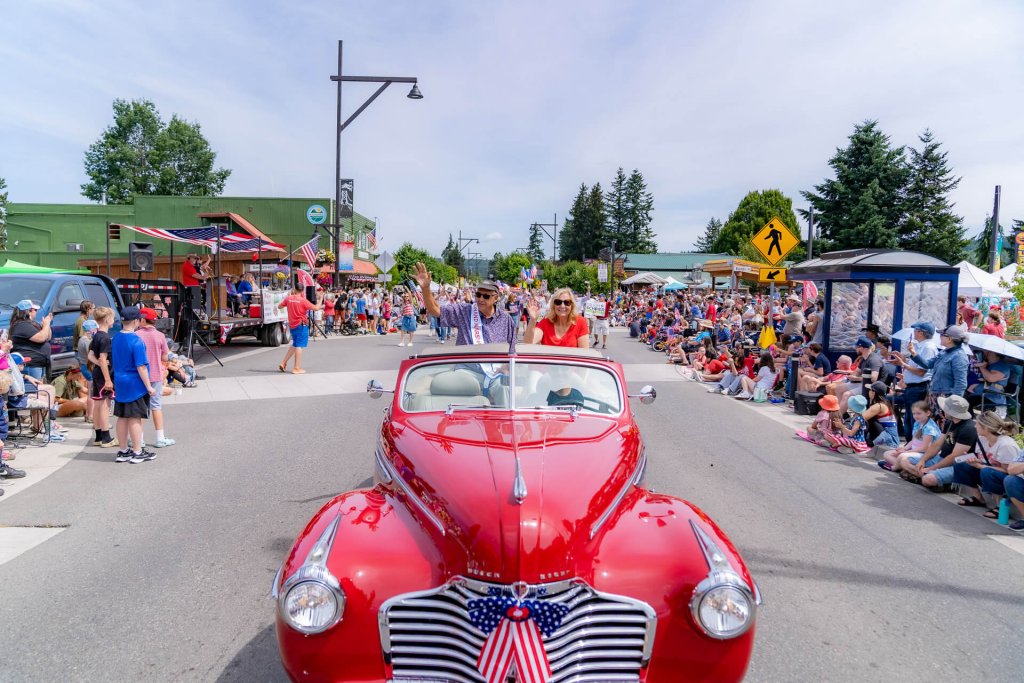 Two people ride in the back of a classic car during a parade