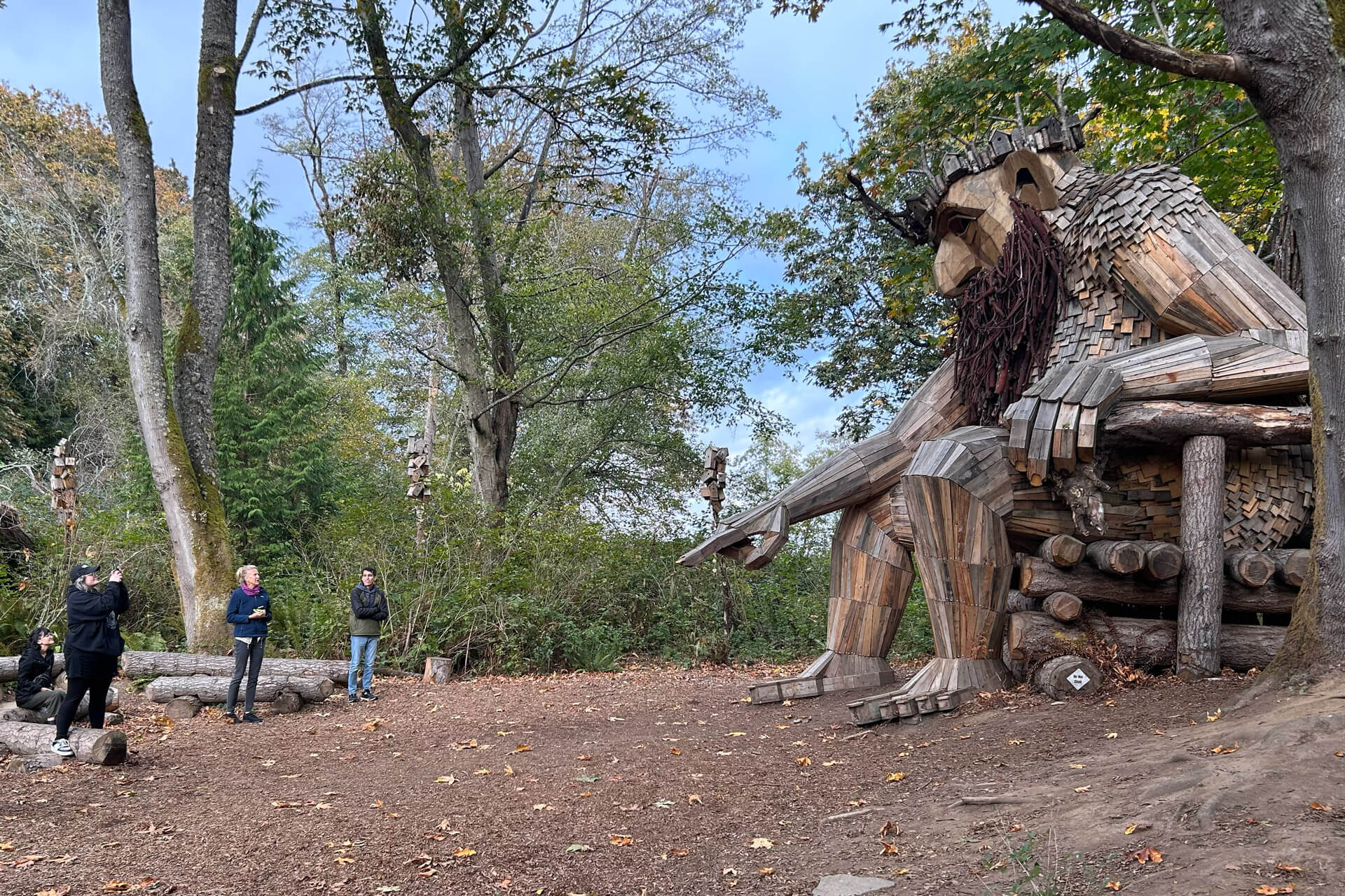 A wooden troll sculpture with a long beard points at the ground
