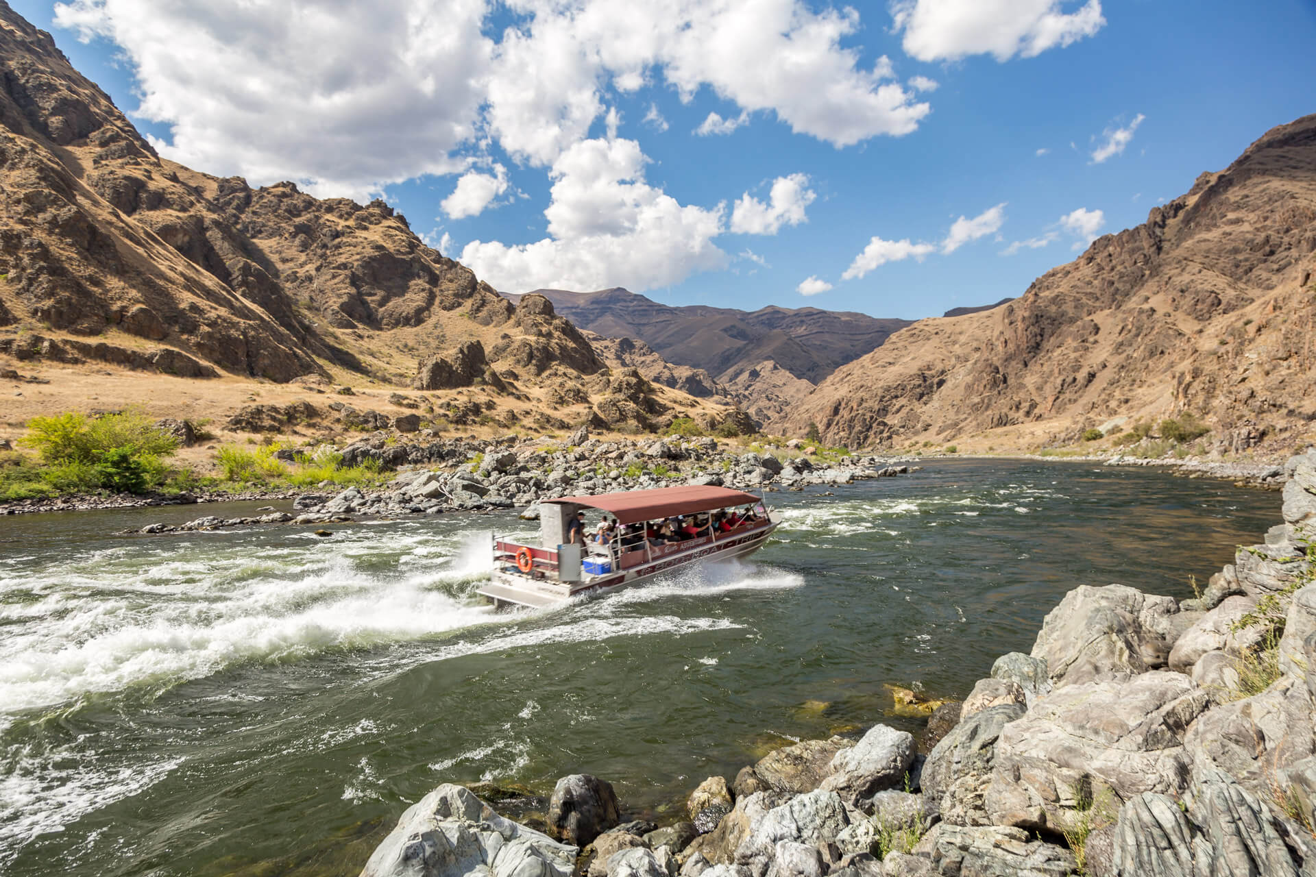 A boat tour heads down a river between brown canyons