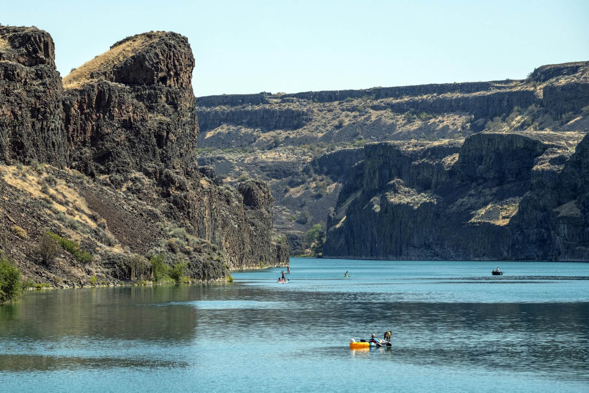 A person kayaks along a body of water surrounded by dry canyon walls